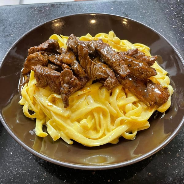 Peruvian Lomo Saltado with fettuccine pasta in a creamy yellow sauce, served in a brown bowl.