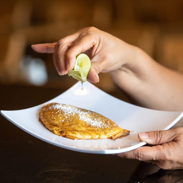Hands squeezing lime over a golden Peruvian picarones dessert dusted with powdered sugar on a white plate.