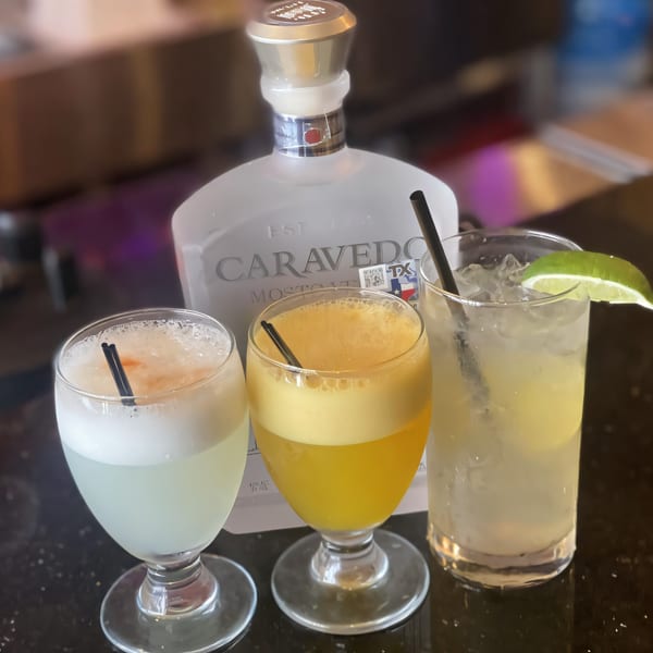 Three Peruvian cocktails, including two Pisco Sours and a clear drink with lime, on a dark bar.