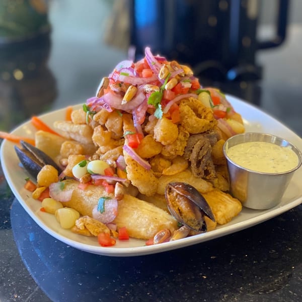 A large platter of Peruvian Jalea Mixta with fried seafood, mussels, red onions, and a side of green sauce.