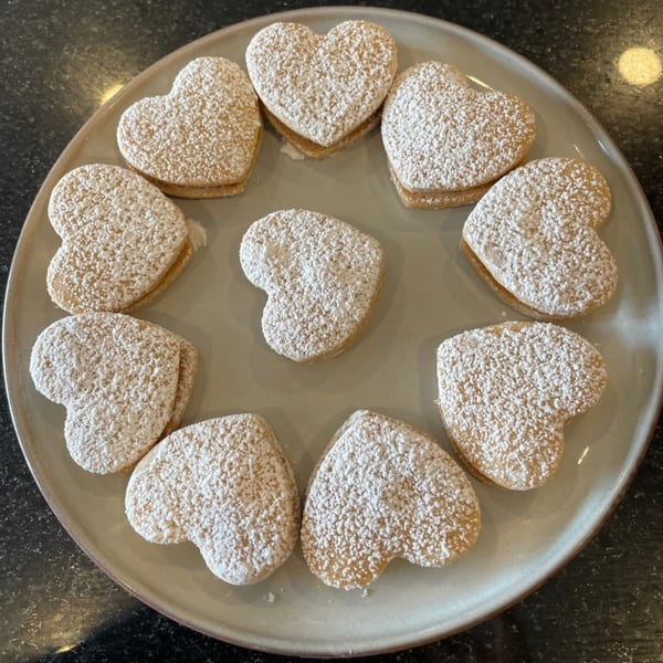 Heart-shaped Peruvian alfajores, dusted with powdered sugar, arranged on a light-colored plate.